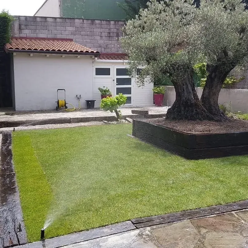 Un aspersor está rociando agua sobre un exuberante césped verde en un patio trasero.