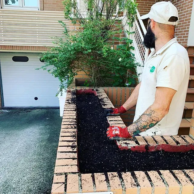 Un hombre con barba está de pie junto a una pared de ladrillos.