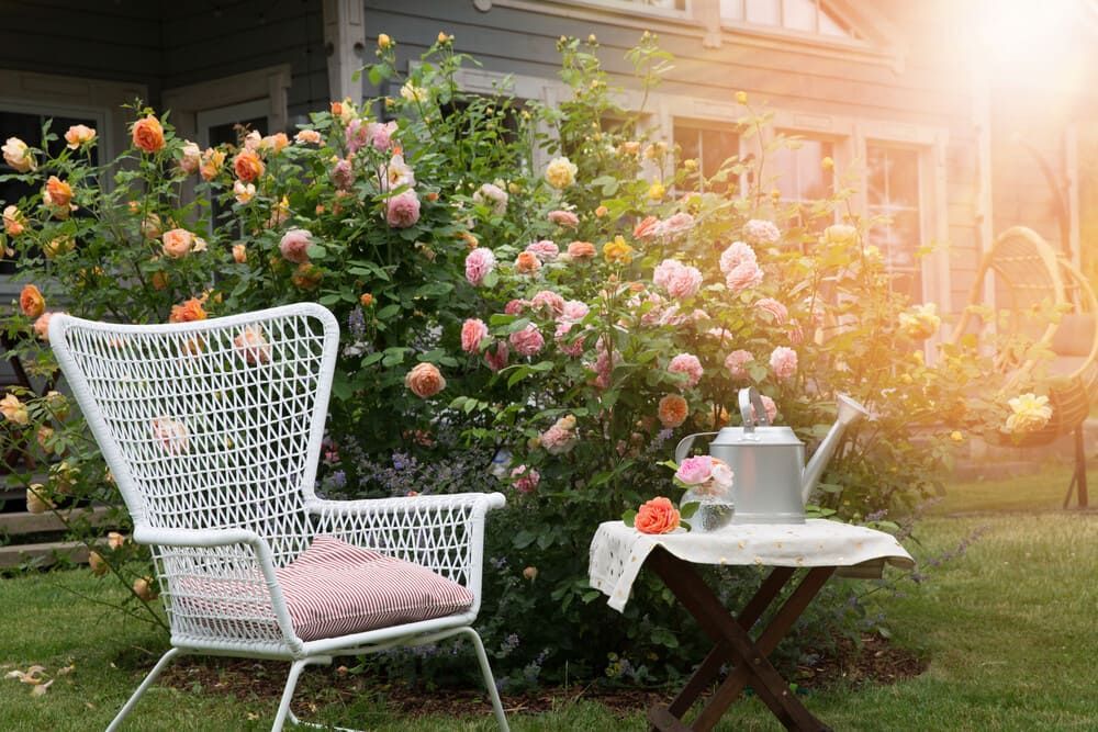 Una silla y una mesa en un jardín con rosas al fondo.