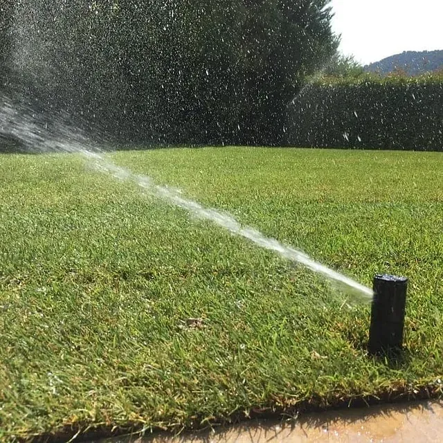 Un aspersor de césped rociando agua sobre un césped verde y exuberante