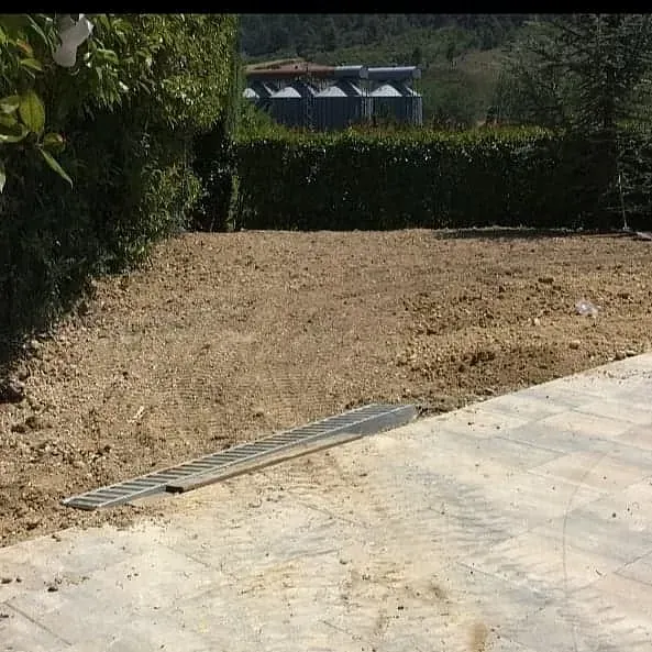 Un campo de tierra con un patio de concreto en primer plano y un seto en el fondo.