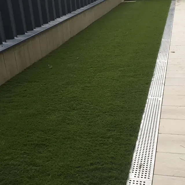 Una acera con césped y un desagüe al costado.