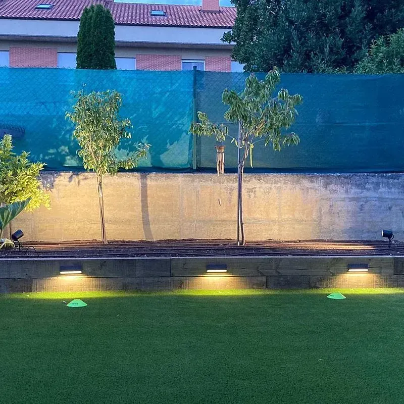 Una valla rodea un exuberante campo verde con árboles y luces.