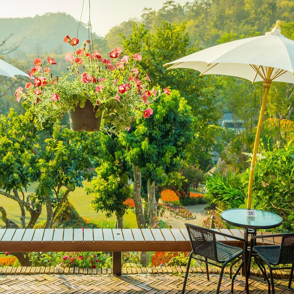 Un patio con un banco, sillas, sombrillas y flores colgando de los árboles.