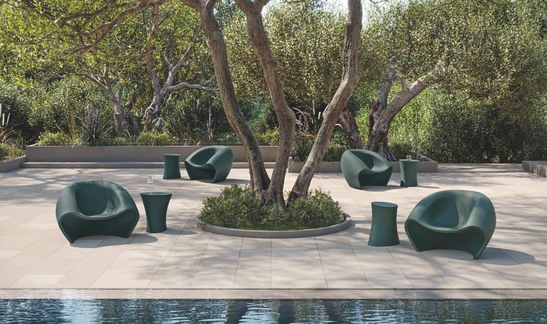 Un grupo de sillas verdes están sentadas debajo de un árbol al lado de una piscina.