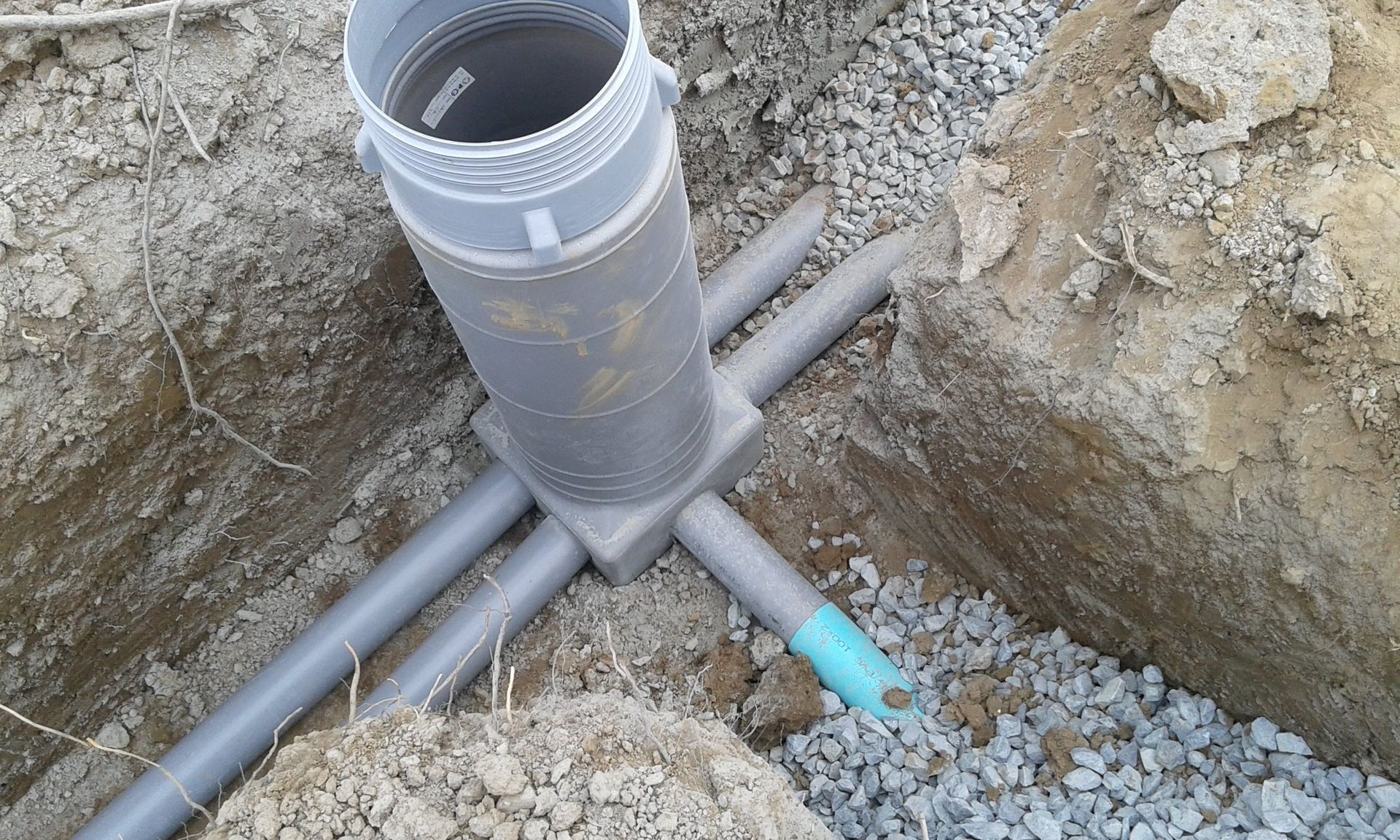 Tuyaux utilitaires en PVC gris raccordés dans une tranchée de terre autour d'une colonne montante verticale