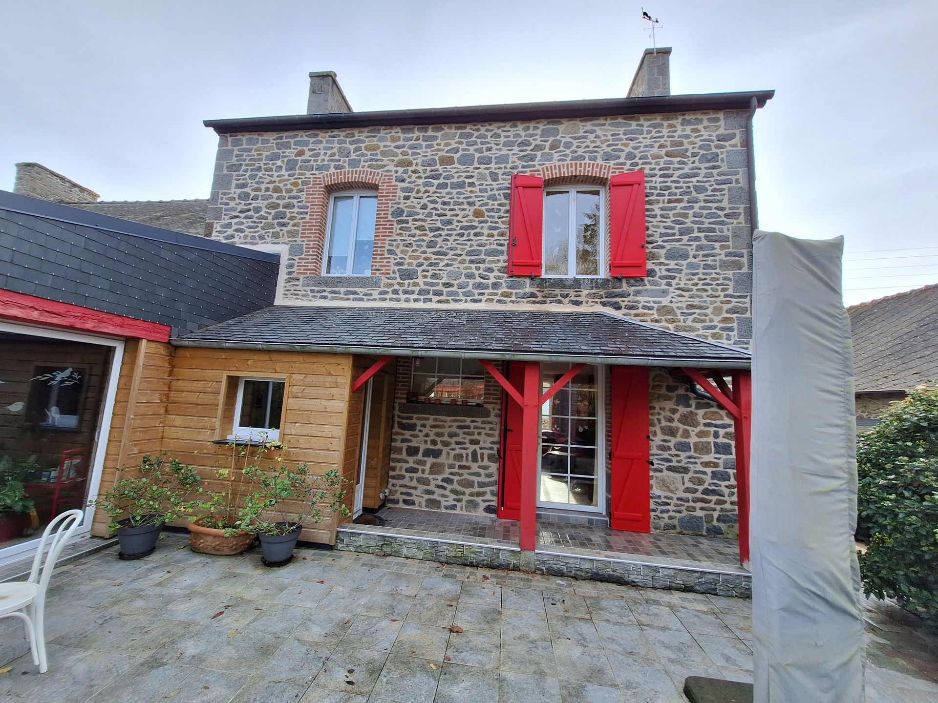 Maison en pierre aux volets et boiseries rouges, vue depuis une cour pavée.