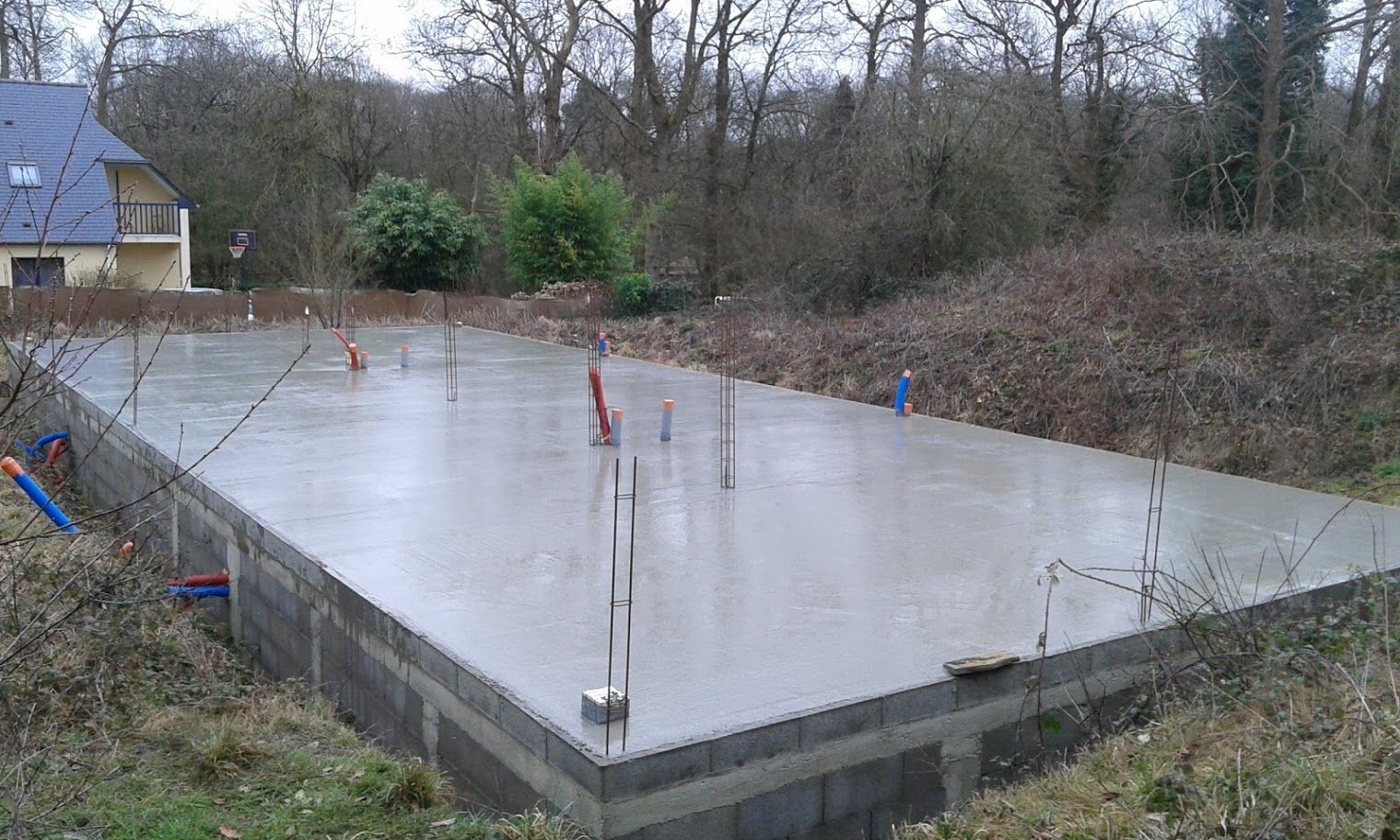 Dalle de fondation en béton frais avec armatures métalliques sur un terrain résidentiel boisé