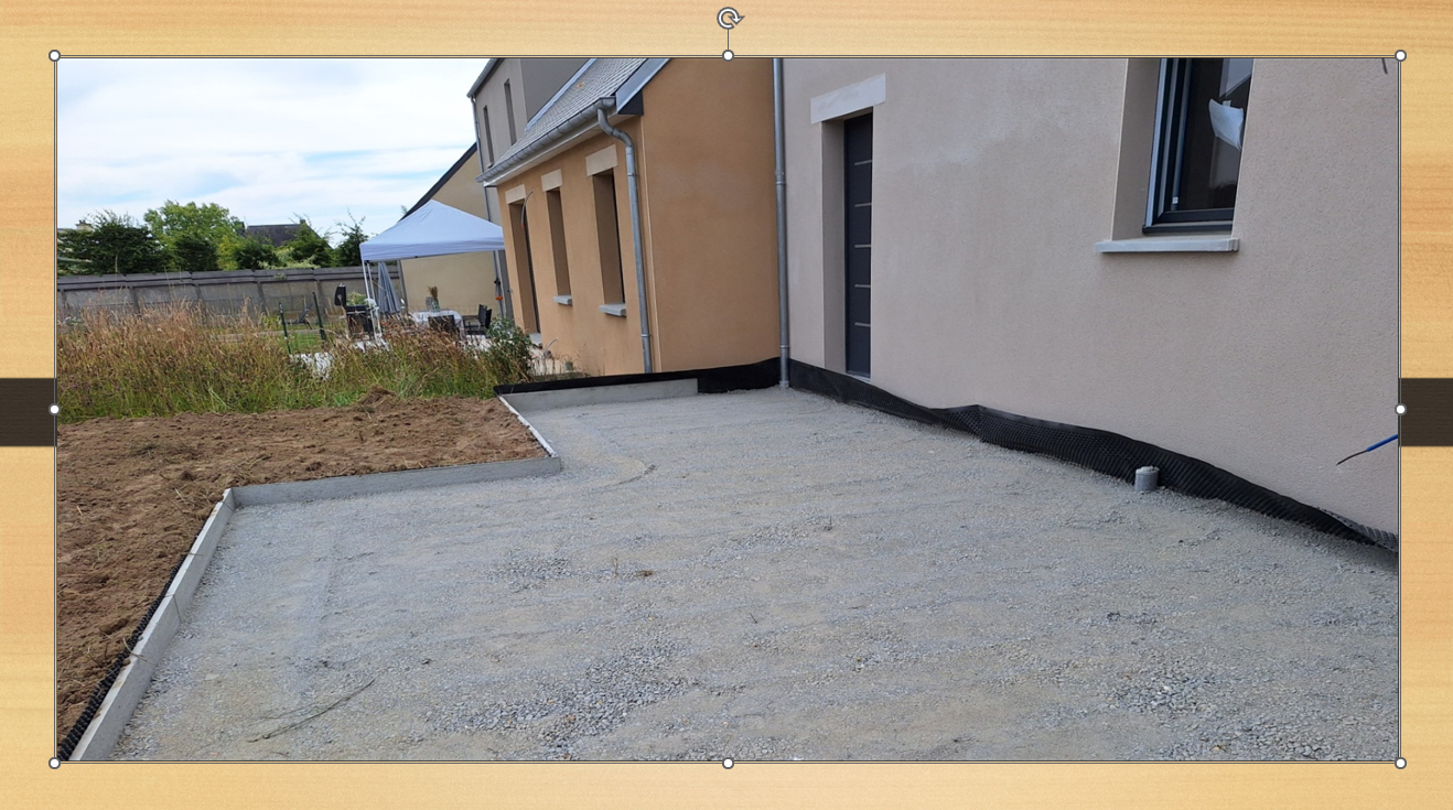 Terrasse en gravier jouxtant une maison beige avec fenêtres et porte d'entrée, bordée par un champ et un ciel nuageux.