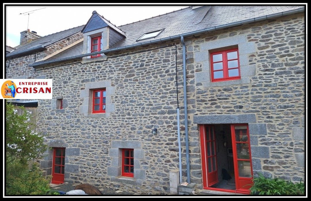 Maison en pierre avec fenêtres et porte à encadrement rouge, portant l'inscription « A TAURO CRISAN » sur le côté gauche.