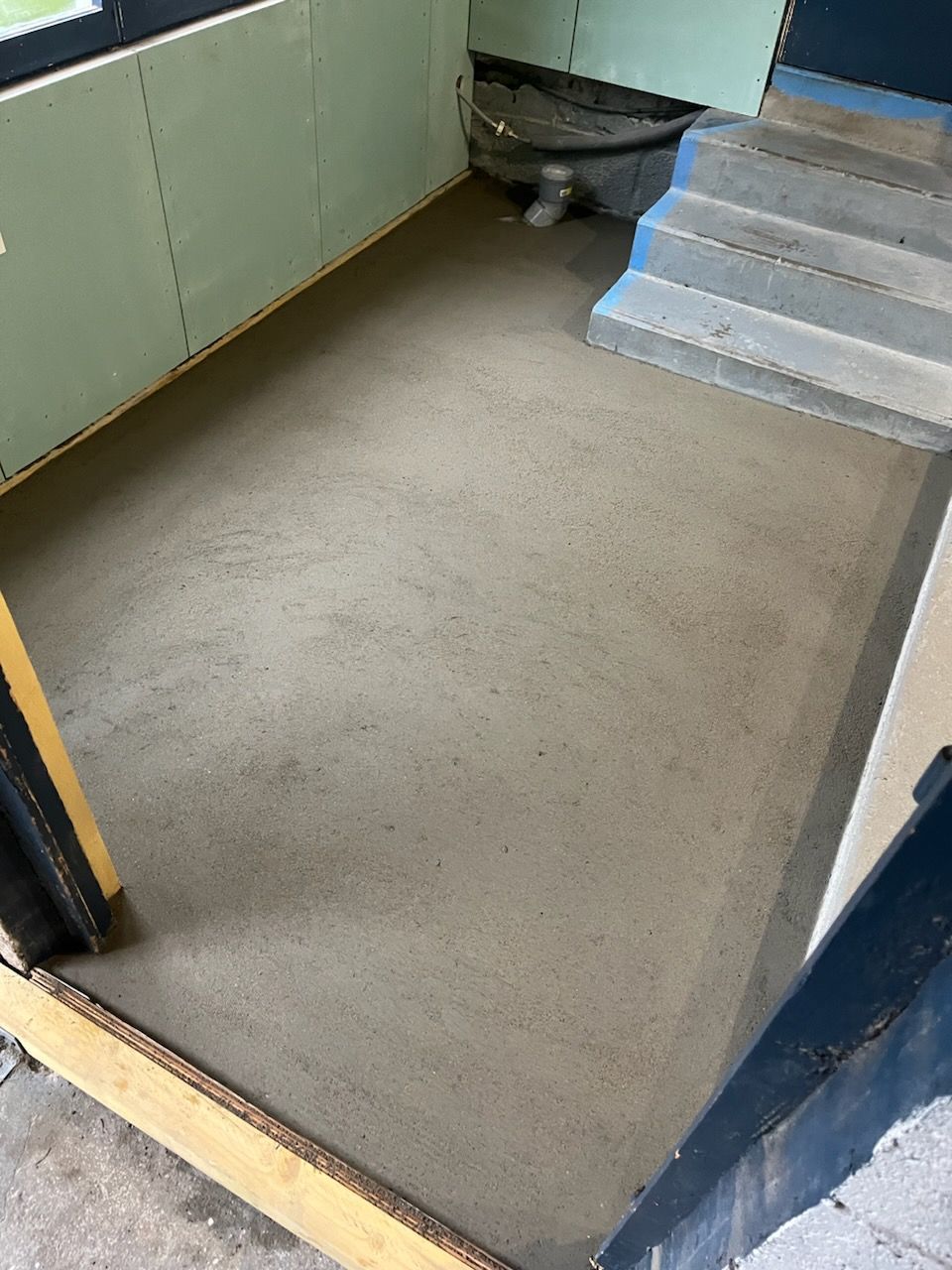 Couloir vide avec sol beige, murs verts et escalier bleu sur la droite.
