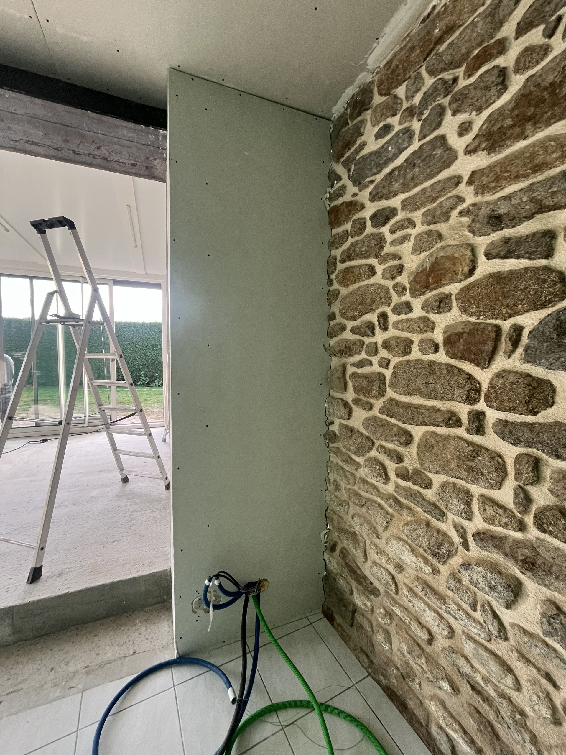 Mur intérieur en pierre et enduit vert, vélo et échafaudage visibles à travers une ouverture
