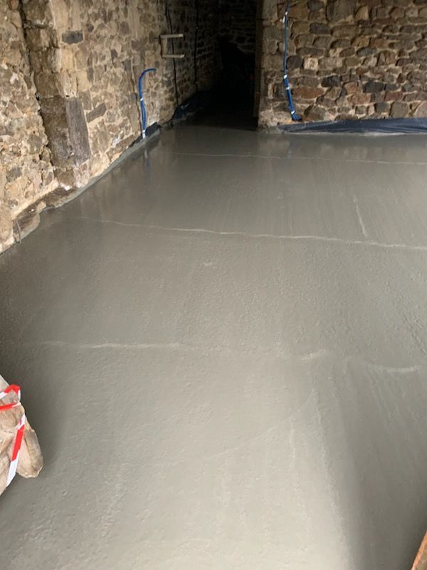 Sol en béton gris fraîchement coulé dans une pièce aux murs de pierre avec une porte sombre