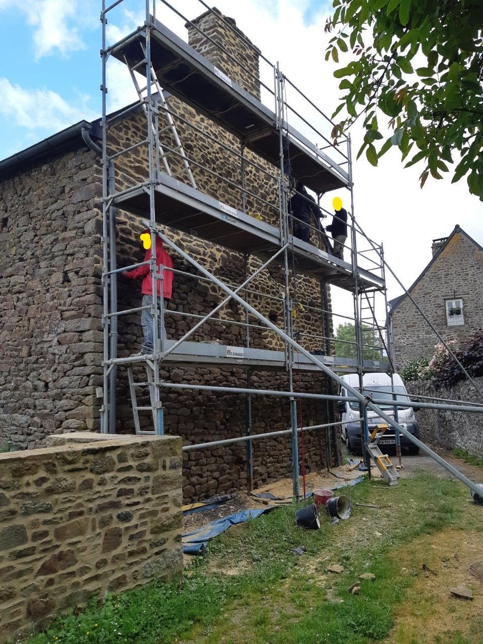 Échafaudage sur un bâtiment en pierre avec deux ouvriers portant des casques de chantier effectuant des réparations extérieures.