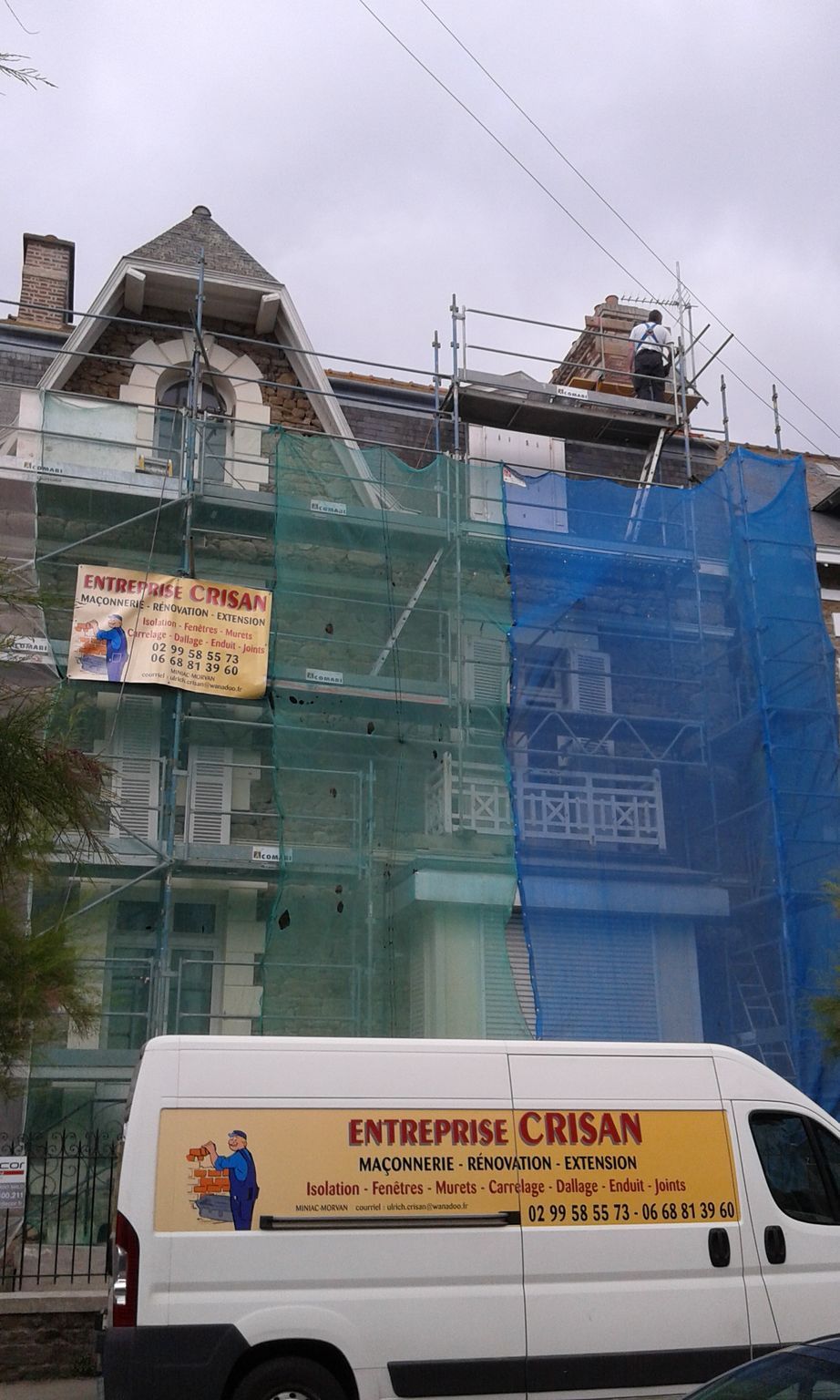 Bâtiment en rénovation avec échafaudages, filets verts et bleus à côté d'une camionnette de livraison blanche.