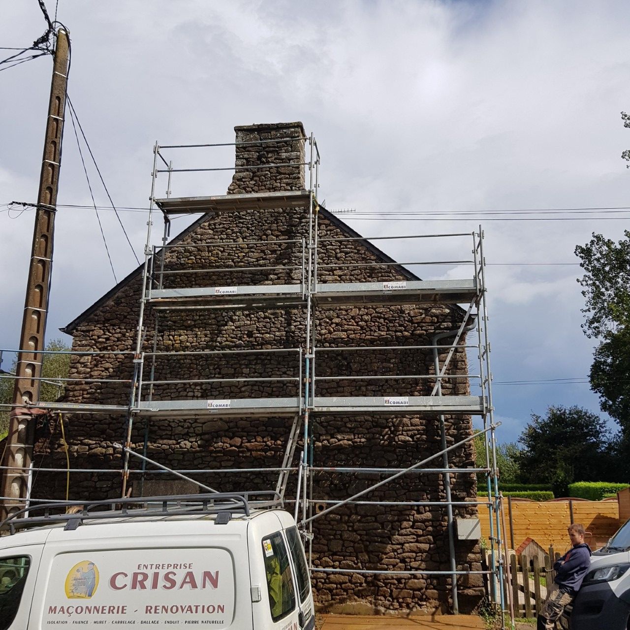 Des échafaudages entourent le clocher en pierre d'une église en cours de rénovation, avec une camionnette utilitaire blanche devant.