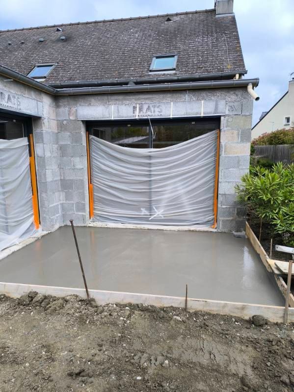 Allée en béton et ouverture de garage en construction, avec une barrière en plastique froissée et une cour avant non finie.