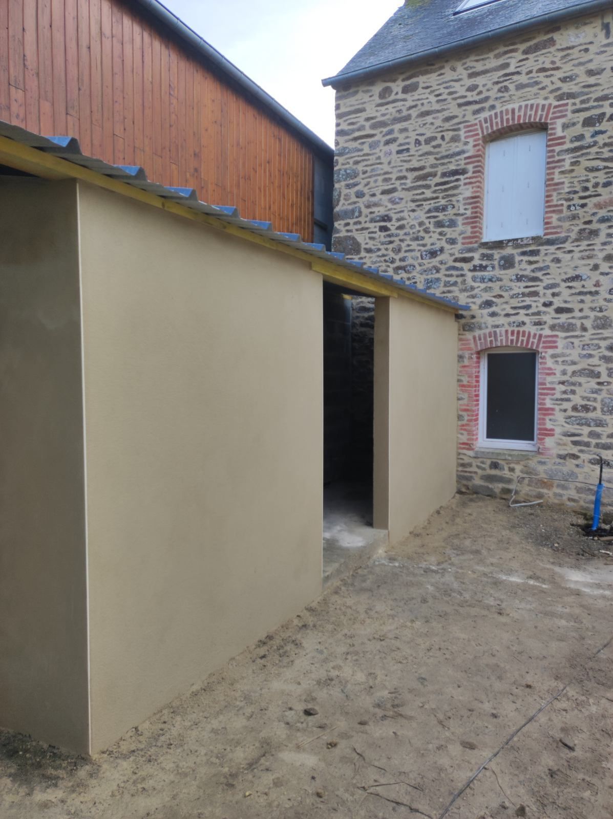 Cour étroite aux murs beiges jouxtant un bâtiment en pierre et un sol gravillonné.