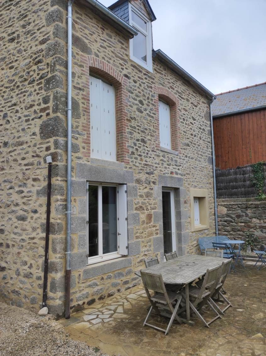 Terrasse en pierre avec une table et des chaises pliantes le long d'un mur et de fenêtres