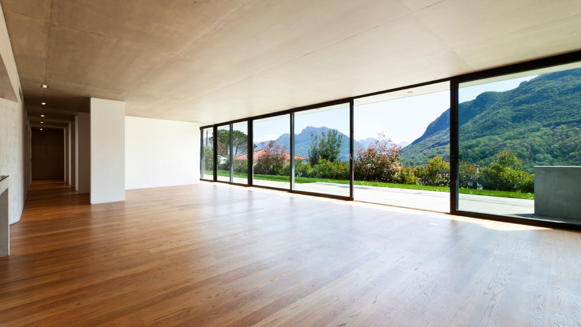Habitación vacía con suelo de madera y grandes ventanales con vistas a las montañas.