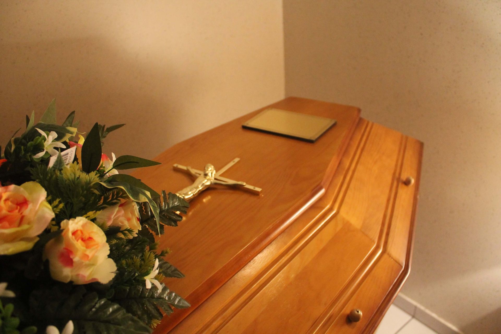 Cercueil en bois avec crucifix et composition florale.