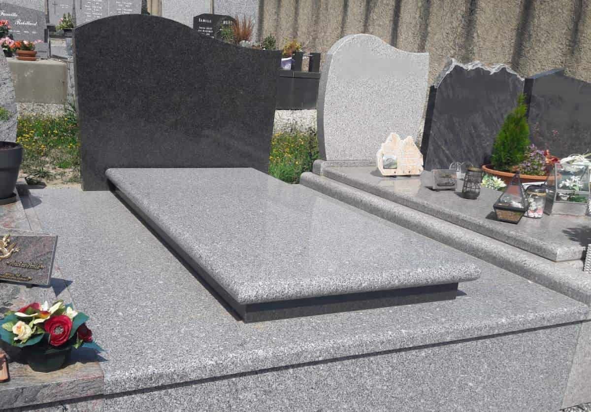 Pierre tombale et socle en granit gris dans un cimetière.