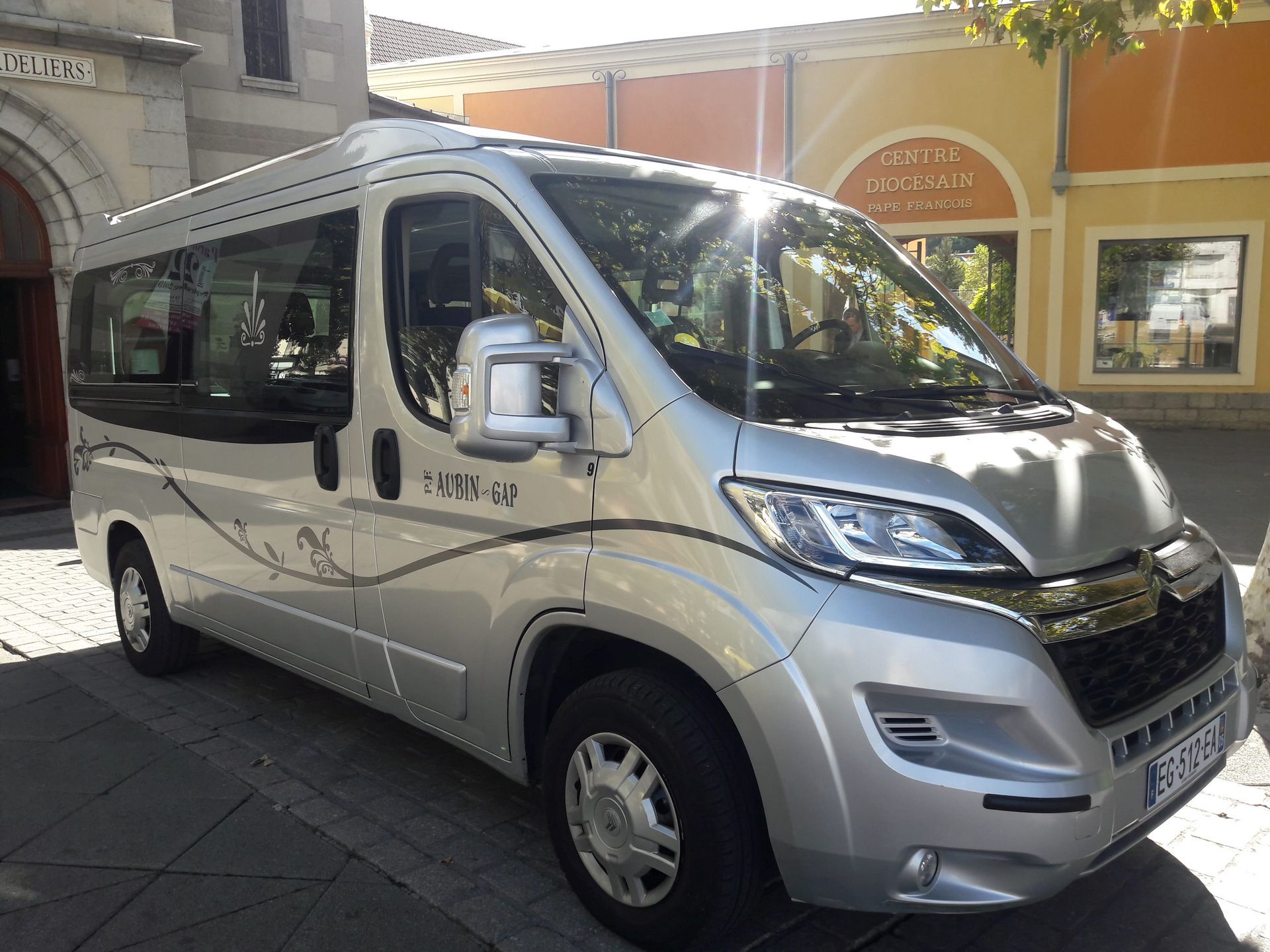 Un camping-car argenté est garé près d'un bâtiment dont l'entrée ressemble à celle d'une église. Journée ensoleillée.