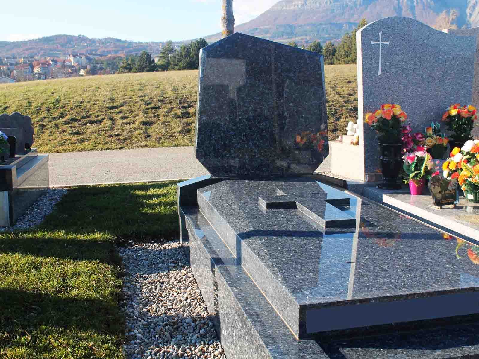 Pierre tombale en granit gris avec croix et fleurs dans un cimetière.