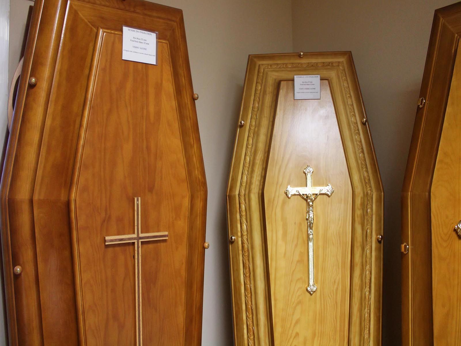 Des cercueils en bois ornés de croix en or sont exposés dans une maison funéraire.