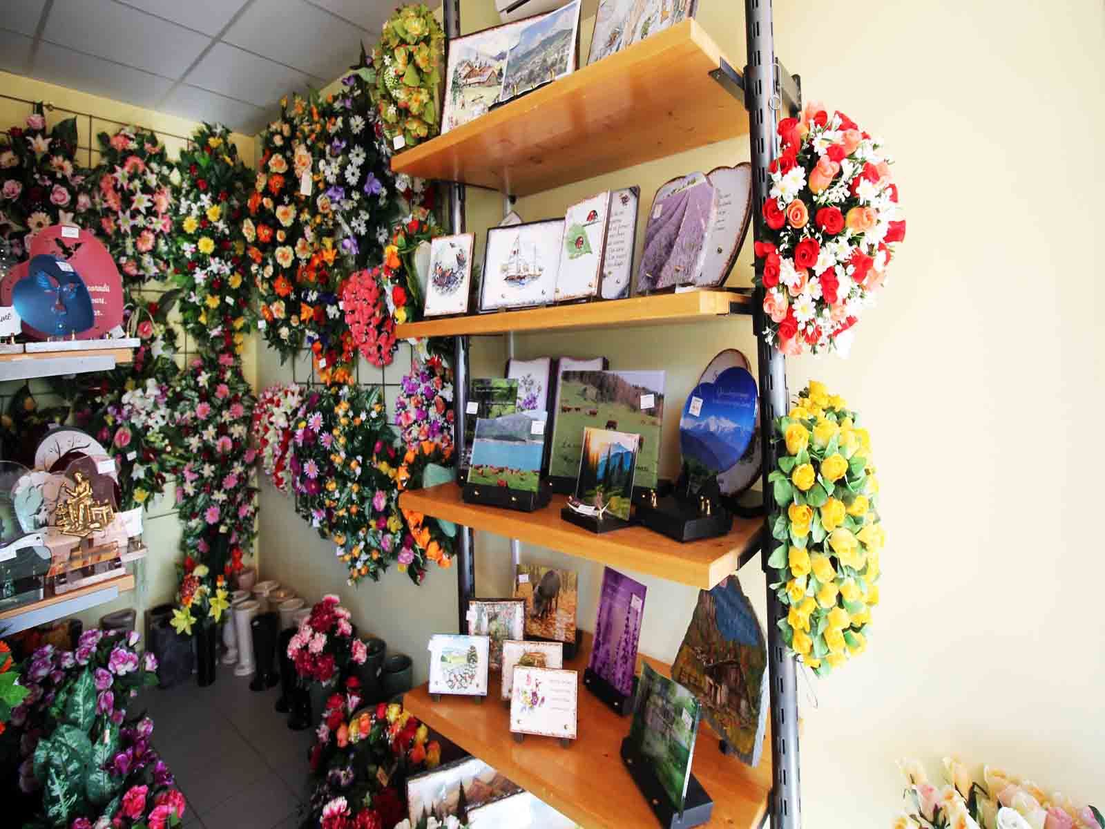 Intérieur d'une boutique de fleurs avec des étagères présentant des couronnes de fleurs et des cartes encadrées.