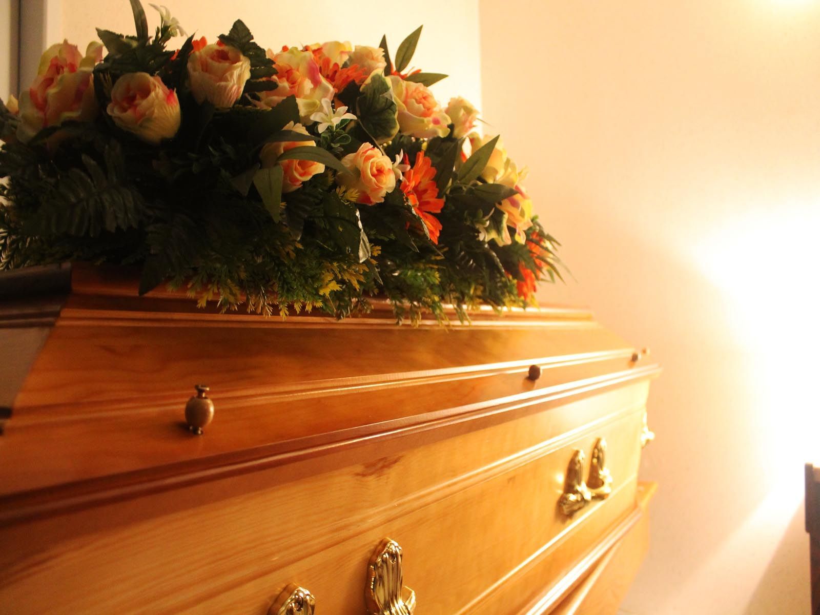 Un cercueil en bois orné d'une composition florale dans une pièce baignée de lumière.