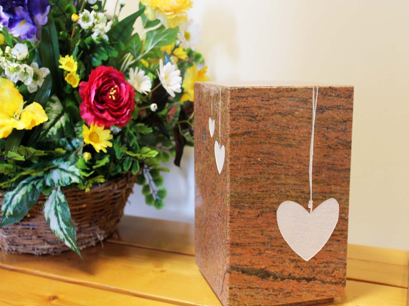 Une urne funéraire en granit ornée de cœurs en papier, à côté d'un arrangement floral.