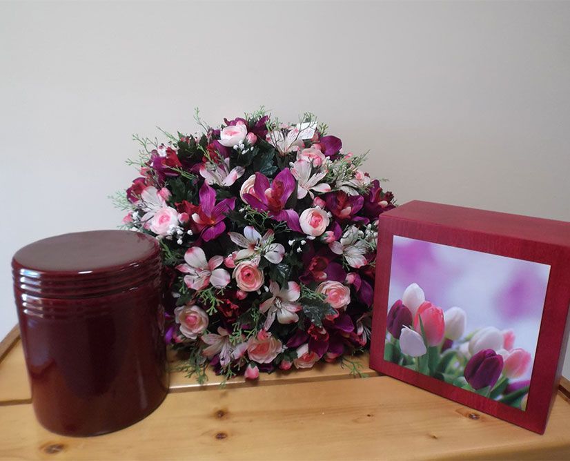 Urne et boîte rouges contenant un arrangement floral, probablement pour un hommage.