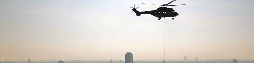 Ein Hubschrauber, an dem ein Seil befestigt ist, fliegt über einer Stadt.