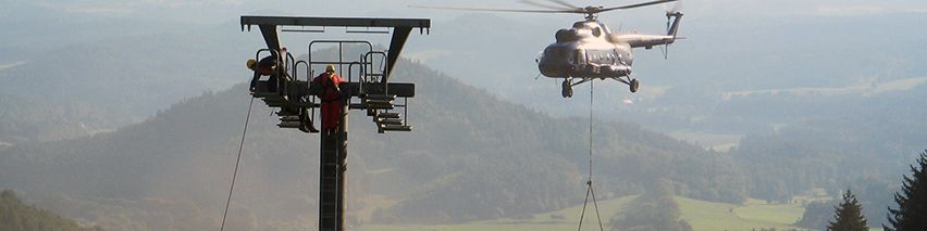 Ein Hubschrauber fliegt über einen Skilift in den Bergen.