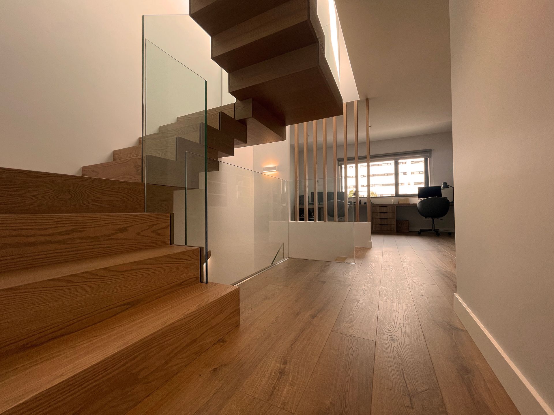 Una escalera de madera con barandilla de vidrio en un pasillo.