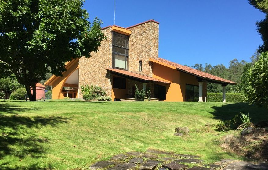 Una casa grande con techo de tejas rojas está rodeada de césped y árboles.
