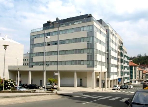 Un gran edificio blanco con muchas ventanas y coches aparcados delante.