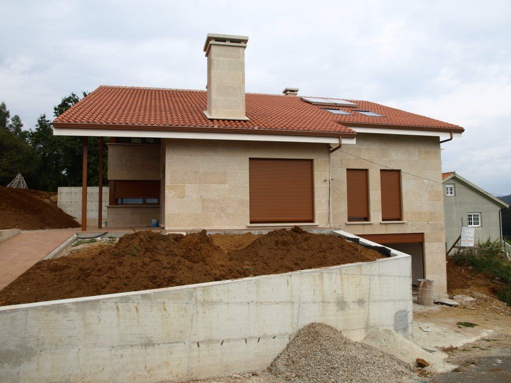 Una casa con techo de tejas rojas y contraventanas en las ventanas