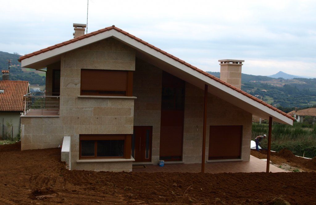 Una casa con techo de tejas rojas está situada en medio de un campo de tierra.