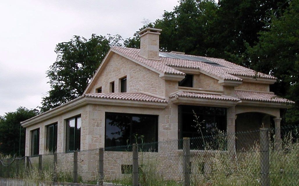 Una casa con techo de tejas está rodeada de hierba alta y árboles.
