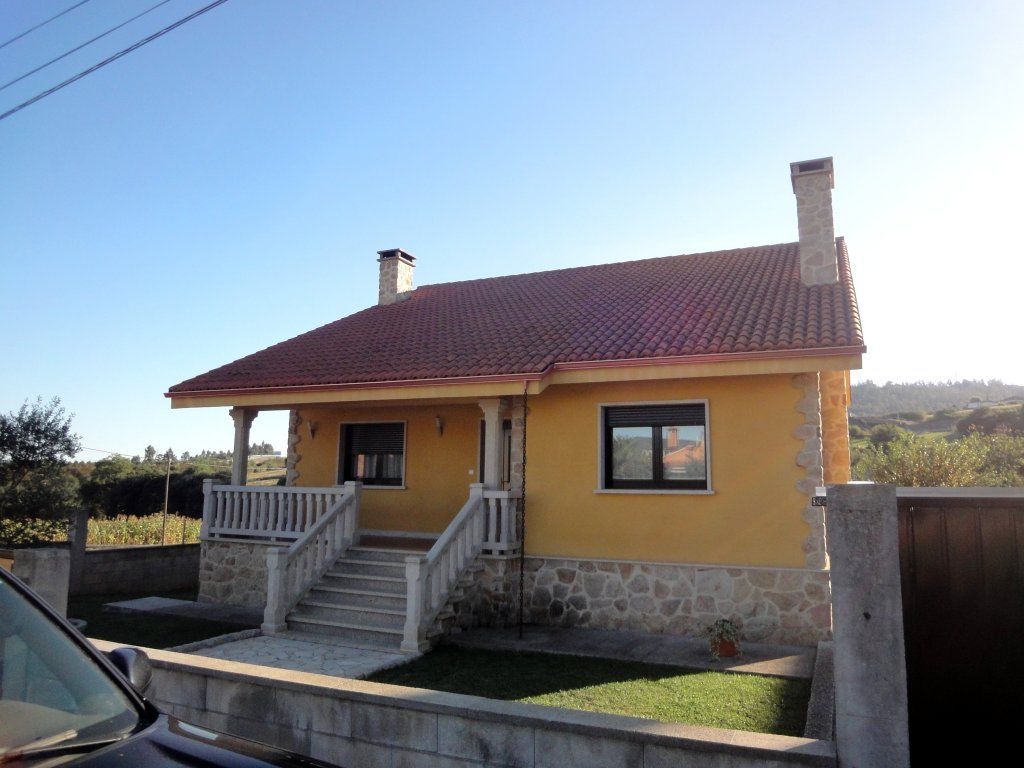 Una casa amarilla con techo de tejas rojas y un coche aparcado delante de ella.