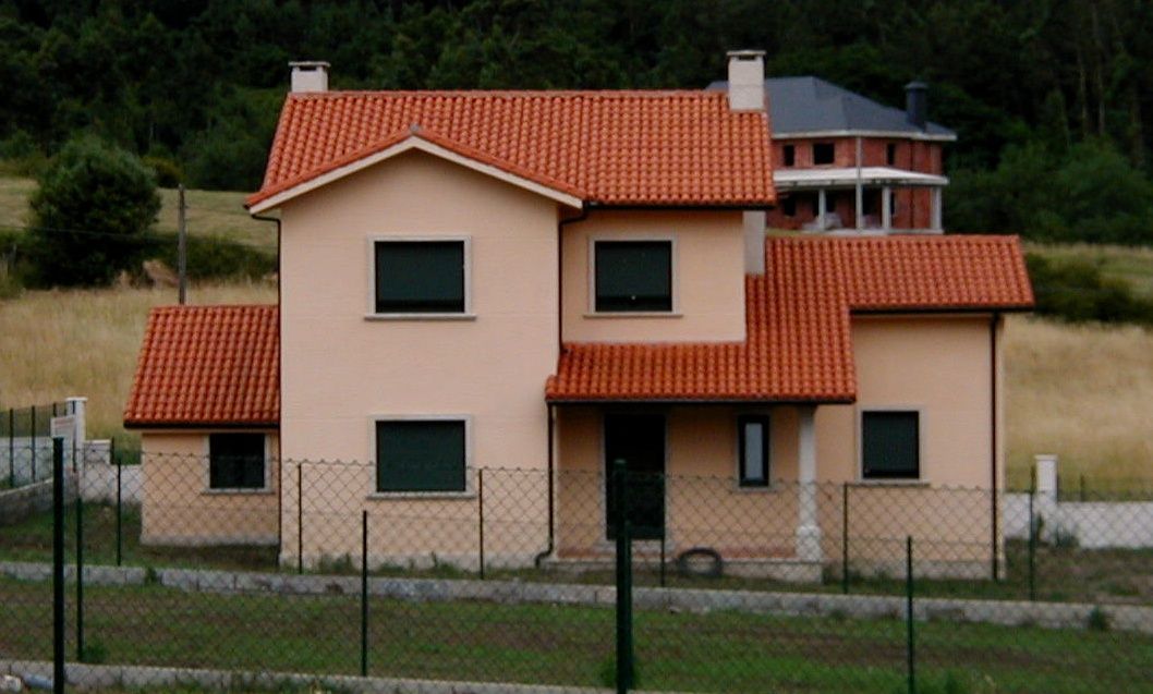 Una casa con techo de tejas rojas y una valla alrededor