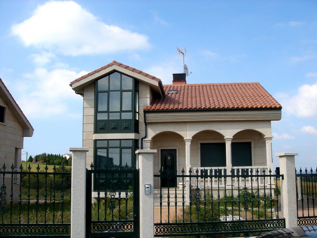 Una casa con techo de tejas rojas está detrás de una valla de hierro forjado.