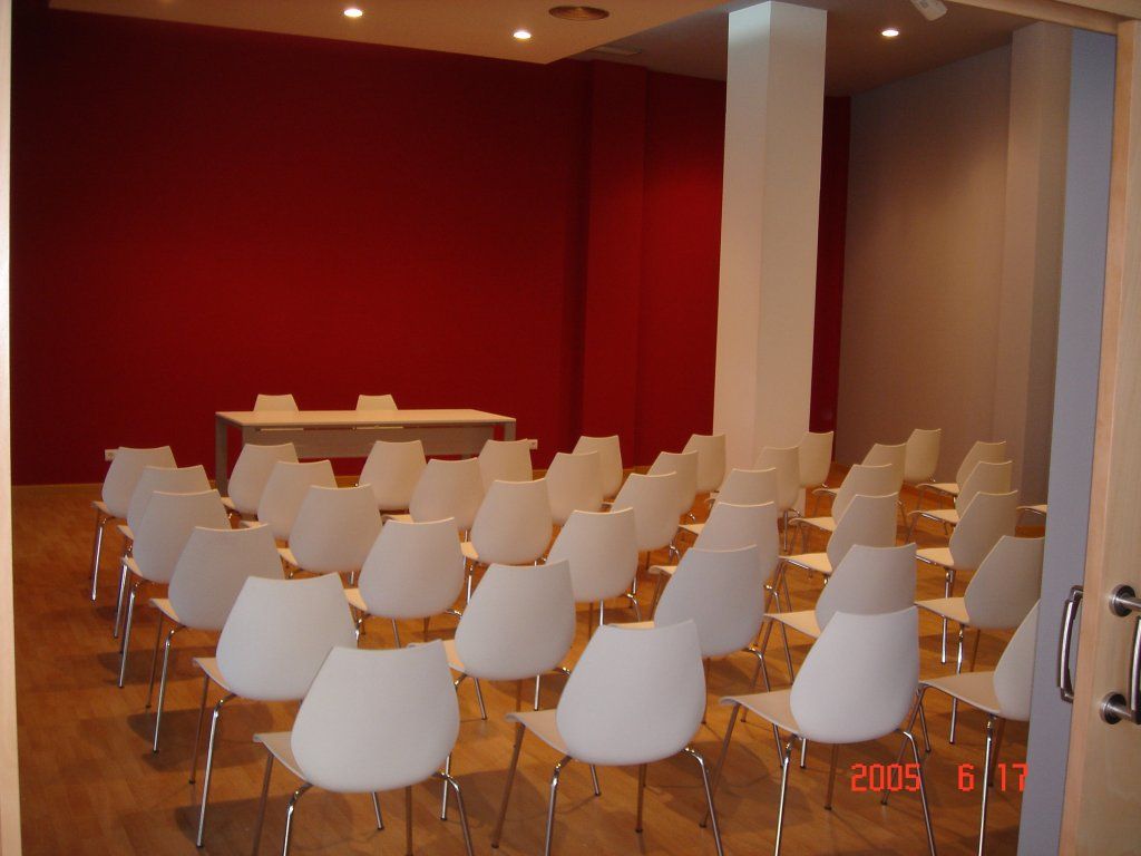 Filas de sillas blancas están alineadas en una habitación con una pared roja.