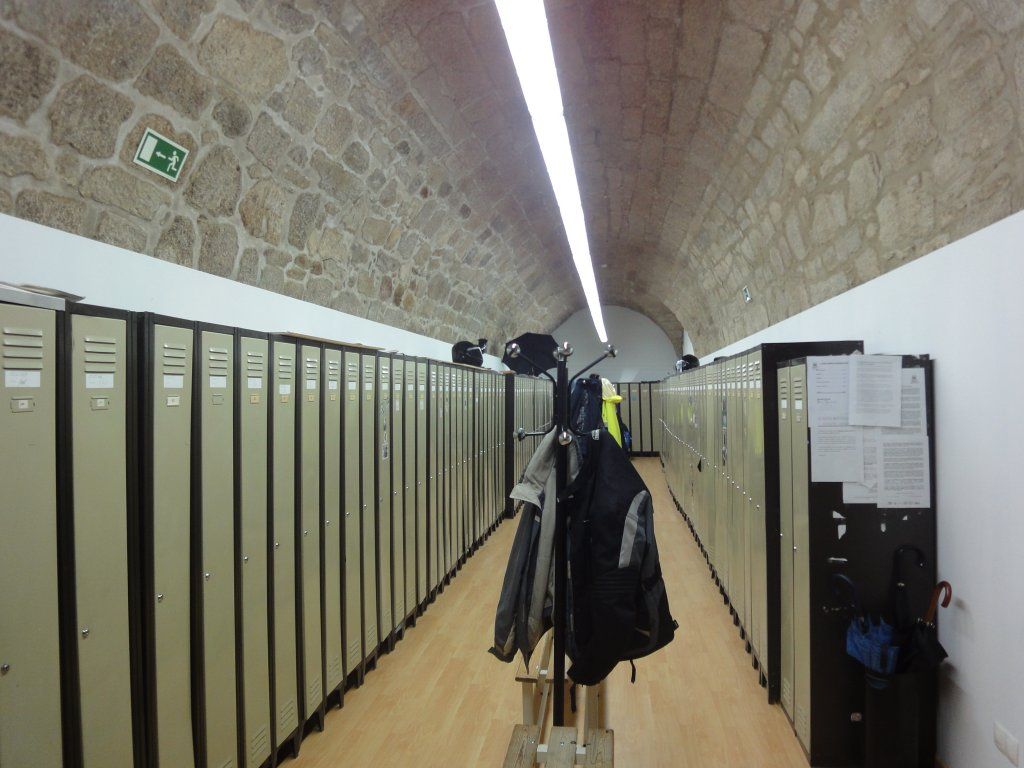 Un largo pasillo de casilleros con una señal de salida verde en la pared.