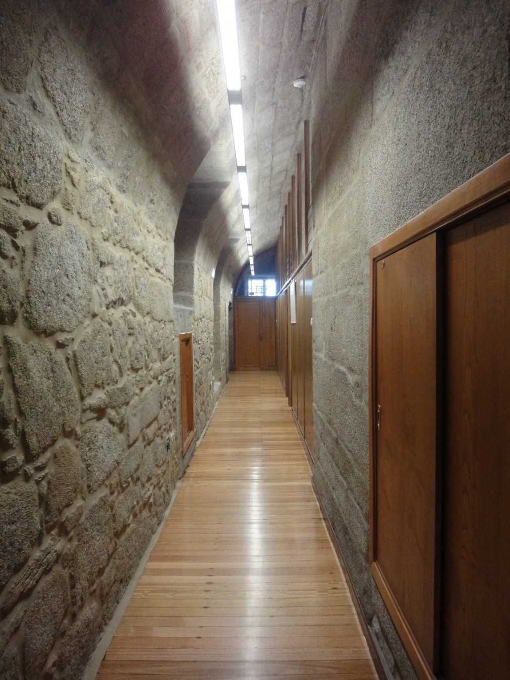 Un largo pasillo con suelos de madera y paredes de piedra.