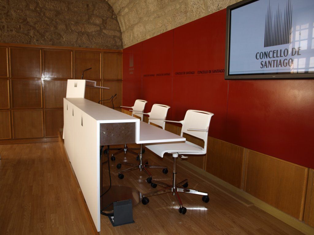 Una sala con un podio y sillas y un cartel que dice Concello de Santiago.