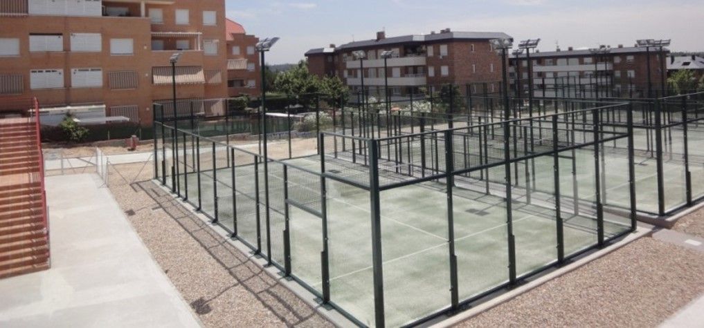 Una cancha de tenis con una valla alrededor y un edificio al fondo.
