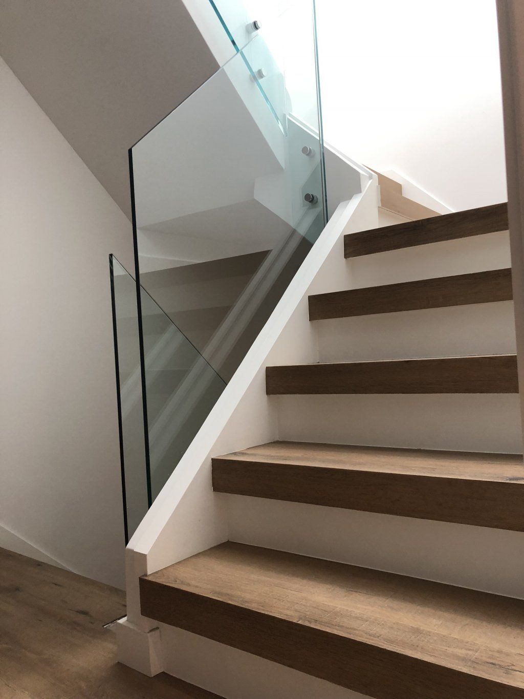 Una escalera con escalones de madera y barandilla de cristal.